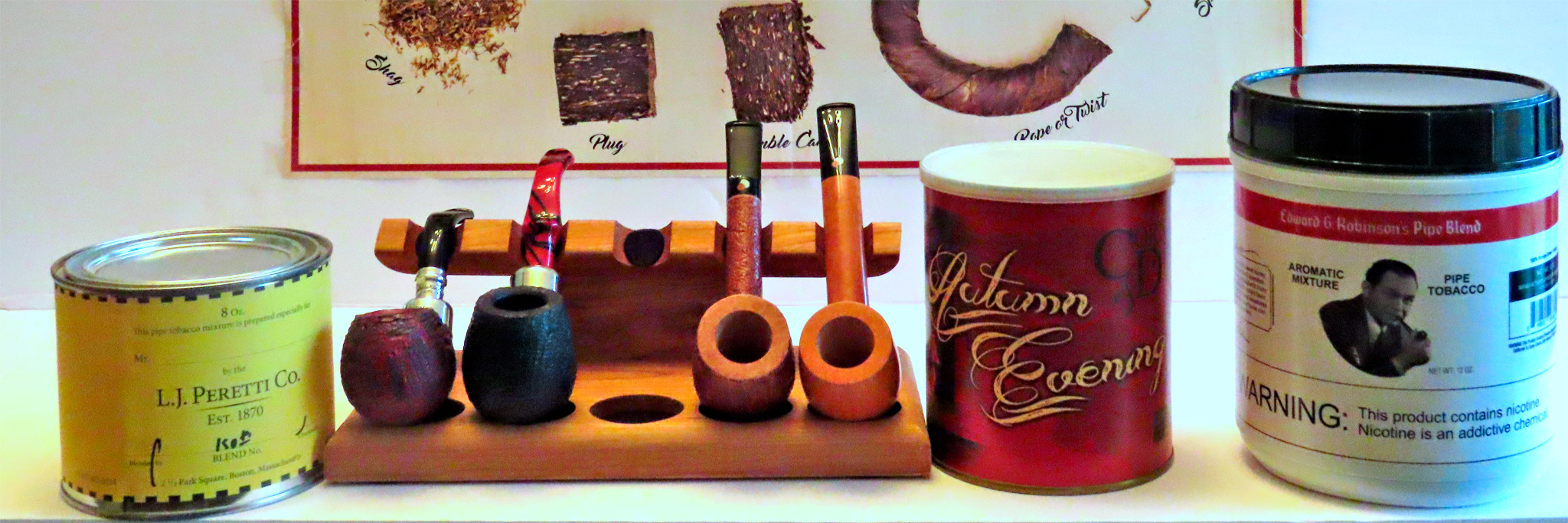 Some favored tobacco blends and new pipes from left: L.J. Peretti 150th Anniversary Virginia Flake blend; new pipes L-R: Peterson XL02 Rua Fishtail (red fox) in a crimson-and-black contrast-stained sandblast and the Peterson Halloween 2021 System Pipe B42 P-Lip with its acrylic red and black stem and black sandblast; two Claudio Cavicchis, L-R, Lovat brown sandblast and CCC Canadian; two tobacco cans, Cornell & Diehl’s Autumn Evening and Sutliff Tobacco Co.’s Edward G. Robinson’s Pipe Blend. Photo by Fred Brown