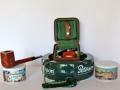 From L-R: The Rich Lewis Custom Bill NASPC 2014 POY atop a fresh tin of Low County Atalaya a ready-rubbed blend combining Red and Bright Virginias from 2019 with C&D's proprietary Red Virginia Cavendish. Peterson’s Grafton System Pipe Travel Case specifically designed for Peterson System pipes, with matching leather pipe stand and a green suede tobacco pouch. Front: Peterson's Thinking Man pewter tamper, attributed to Peterson’s 1905 slogan, "The Thinking Man Smokes a Peterson Pipe." Far right: Fresh tin of C&D Low Country Edisto blend, Red Virginias pressed and sliced into flakes. Photo by Fred Brown